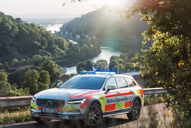 Notarzt-Einsatzfahrzeug mit blauem Blinklicht auf einer Höhenstraße über dem Neckartal, im Gegenlicht dahinter die Flusskrümmung und die Hänge des Odenwalds.