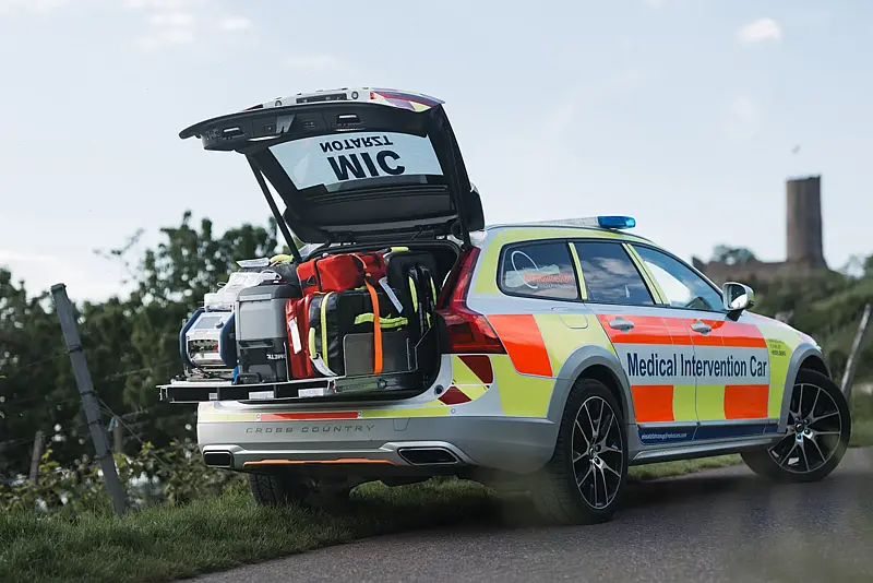 Notarztfahrzeug mit geöffneter Heckklappe am Straßenrand, auf der ausgezogenen Ladefläche Notfallrucksäcke und Medizintechnik, dahinter ein Burgturm auf dem Hügel.