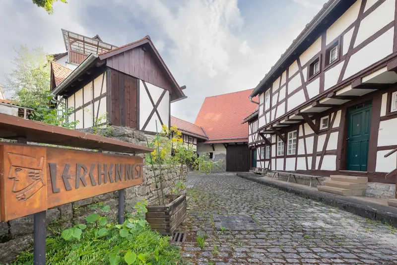 Gepflasterte Gasse zwischen Fachwerkhäusern im Kraichgau, links ein geschnitztes Holzschild, rechts eine grüne Haustür unter weiß-braunem Fachwerk.