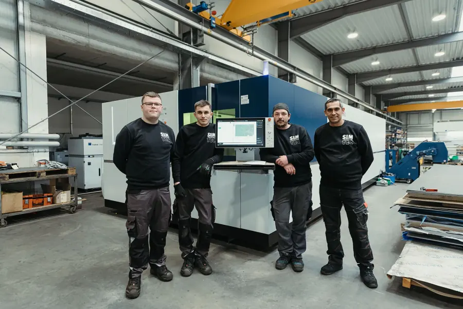 Vier Mitarbeiter vor der Laserschneidanlage in der Fertigungshalle