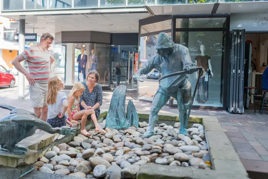 Familie sitzt am Brunnen mit Bronzefiguren in der Sinsheimer Fußgängerzone und betrachtet die Figur des Fischers.